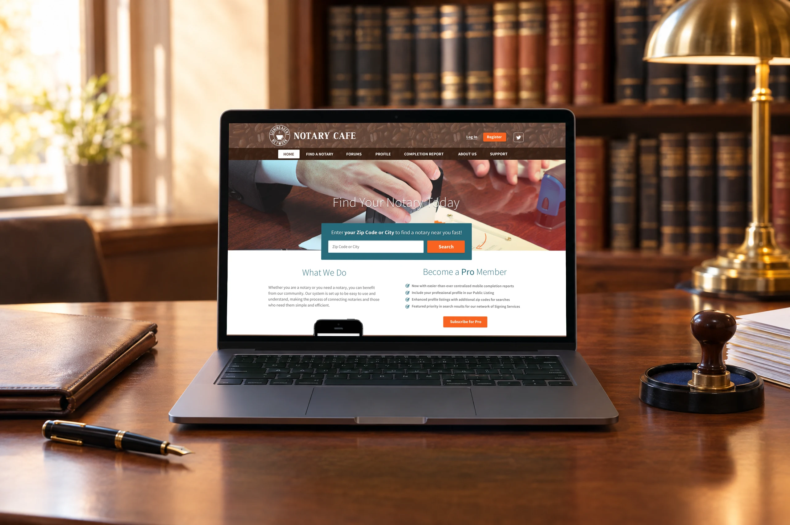Notary Cafe's homepage on a laptop on a walnut desk in a notary's office: a leather folder, a fountain pen, a stamp and law books around it